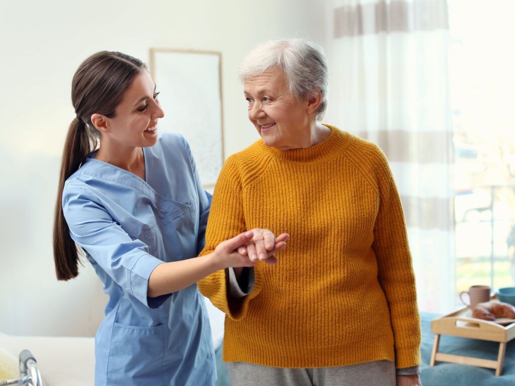A live-in carer holds the hand of an older adult to guide her and support her to mobilise safely.  Both are happy and making eye contact with each other that shows trust has been built between them.